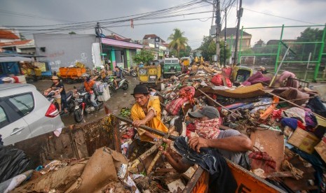 Petugas memindahkan sampah yang menumpuk di sisi jalan pascabanjir 