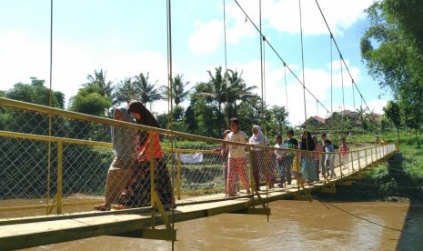 Warga melintas di jembatan gantung yang menghubungkan Desa Sukasenang, Kecamatan Banyuresmi, dan Kelurahan Lengkongjaya, Kecamatan Karangpawitan, Kabupaten Garut, Ahad (26/1). Sebelum adanya jembatan itu, warga harus menggunakan rakit untuk menyeberangi Sungai Cimanuk.