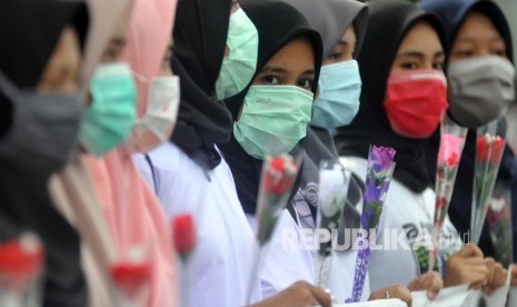 Sejumlah mahasiswi memegang bunga mawar dan menggunakan masker sambil memperlihatkan spanduk kampanye Anti Kekerasan Seksual Terhadap Perempuan, di Padang, Sumatera Barat, Ahad (16/2/2020). 