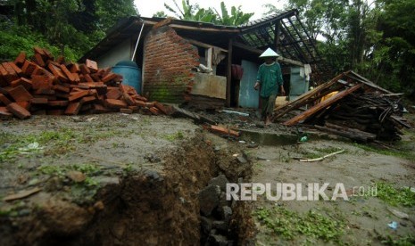 Warga berjalan di depan sebuah rumah yang rusak akibat tanah bergerak. ilustrasi