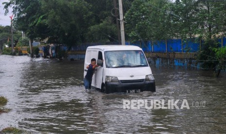 Pengendara mendorong mobilnya yang mogok karena menerobos banjir di Pulogadung, Jakarta Timur, Ahad (23/2/2020).