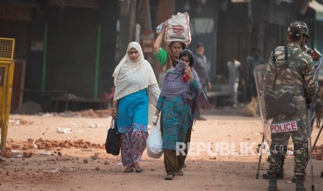 Wanita berjalan melewati tentara Paramiliter India yang berjaga-jaga di daerah yang menyaksikan kekerasan pada hari Selasa di New Delhi, India, Rabu, 26 Februari 2020.