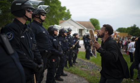 Seorang demonstran berhadapan dengan polisi di rumah petugas kepolisian Minneapolis Derek Chauvin yang dipecat pada Rabu (27/5). Walikota Minneapolis menelepon hari Rabu untuk tuduhan kriminal terhadap petugas polisi kulit putih yang terlihat di video berlutut di leher Floyd George, seorang pria kulit hitam terborgol yang mengeluh bahwa ia tidak bisa bernapas dan meninggal dalam tahanan polisi. Jeff Wheeler / Star Tribune via AP