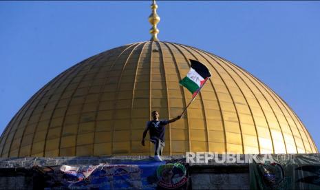 Mantan Pemimpin Hamas Minta Israel Tinggalkan Al Aqsa. Seorang pemuda mengibarkan bendera Palestina dengan latar Masjid Kubah Batu usai melaksanakan sholat Idul Fitri di Kompleks Masjid Al Aqsa, Yerusalem, Kamis (13/5).  