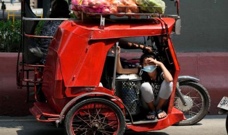 Seorang gadis mengenakan masker untuk mencegah penyebaran virus corona naik becak dengan kantong sayuran pada Selasa, 8 Maret 2022 di Manila, Filipina. 