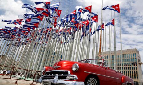 Sebuah mobil konvertibel Amerika klasik melintas di samping kedutaan Amerika Serikat saat bendera Kuba berkibar di Anti-Imperialis Tribune, sebuah panggung besar di promenade pantai Malecon di Havana, Kuba, 26 Juli 2015. Kedutaan Besar Amerika Serikat di Kuba membuka visa dan layanan konsuler pada hari Rabu, 4 Januari 2023. Ini adalah pertama kalinya sejak serentetan insiden kesehatan yang tidak dapat dijelaskan di antara staf diplomatik pada tahun 2017 memangkas kehadiran Amerika di Havana