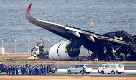 Penyidik ??polisi berkumpul di samping puing-puing pesawat Japan Airlines yang terbakar di bandara Haneda pada Kamis, 4 Januari 2024, di Tokyo, Jepang. Transkrip komunikasi antara pengatur lalu lintas dan dua pesawat yang bertabrakan dan terbakar di Bandara Haneda Tokyo menunjukkan bahwa hanya penerbangan penumpang Japan Airlines yang lebih besar yang diberi izin untuk menggunakan landasan tempat pesawat penjaga pantai bersiap lepas landas.