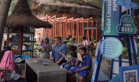 Sekretaris Perusahaan PNM, L Dodot Patria Ary menyimak bacaan salah seorang anak di Pusat Literasi PNM, Pantai Bangsring, Banyuwangi, Kamis (26/9/2024).