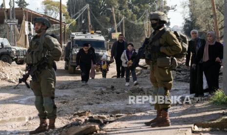 Tentara Israel berjalan di depan warga Palestina yang mengungsi akibat operasi militer Israel dari kamp pengungsi Jenin di Tepi Barat, Kamis, 23 Januari 2025.