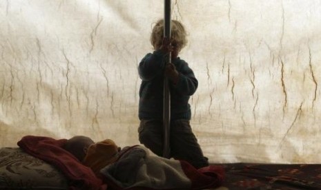 A child hides his face as he sits inside a tent at the Jarjanaz refugee camp in the southern countryside of Idlib November 30, 2014.