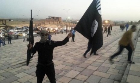 A member of the Islamic State of Iraq and the Syria (ISIS) holds an ISIS flag and a weapon on a street in the city of Mosul, June 23, 2014.