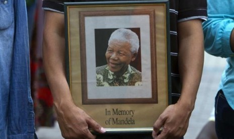 A man holds a tribute photograph as he watches the funeral service for former South African President Nelson Mandela on a large screen television in Cape Town, December 15, 2013.