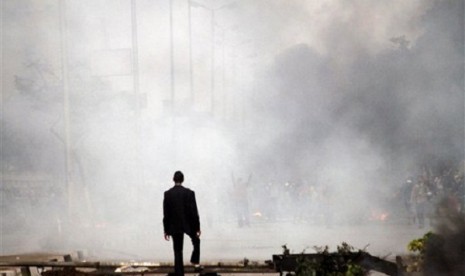 A man stands amid the smoke from tear gas fired by Egyptian riot police in Cairo, Egypt, Friday, Nov. 29, 2013, to disperse hundreds of demonstrators.