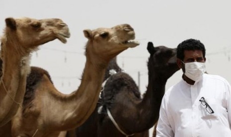 A man wearing a mask looks on as he stands in front of camels at a camel market in the village of al-Thamama near Riyadh May 11, 2014.