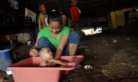 A mother baths her baby in a slum area located under the bridge, where her family live. Uneven wealth distribution in this country still pose a major problem to eradicate poverty. (illustration) 