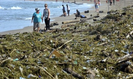 A number of foreign tourits walk near a stack of garbage at Kuta Beach, Bali.  