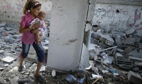 A Palestinian girl holding her sister walks through debris near remains of a mosque, which witnesses said was hit by an Israeli air strike, in Beit Hanoun in the northern Gaza Strip August 25, 2014.