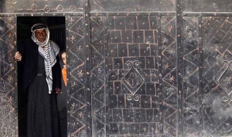 A Palestinian man and girl stand at a doorway and watch as stone-throwing Palestinian protesters clash with Israeli security officers in the West Bank village of Tamoun, near the West Bank city of Jenin January 1, 2013.   