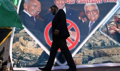 A Palestinian man walks past a poster showing Israeli President Shimon Peres, from left, US Secretary of State John Kerry and Palestinian President Mahmoud Abbas in the northern Gaza Strip, Friday, Feb. 7, 2014.