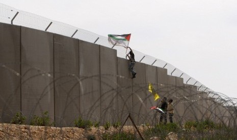 A protester hangs a Palestinian flag on the controversial Israeli barrier during a protest over its construction in the West Bank village of Bilin near Ramallah, recently.