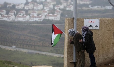 A protester holds the Palestinian flag with the Jewish settlement of Halamish seen in the background during clashes between stone-throwing protesters and Israeli soldiers in the West Bank village of Nabi Saleh, near Ramallah December 21, 2012. (illlustrati