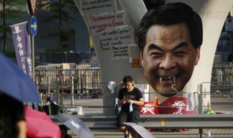 A protester sits next to a defaced cut-out of Hong Kong Chief Executive Leung Chun-ying while blocking a street outside the government headquarters in Hong Kong September 30, 2014. 