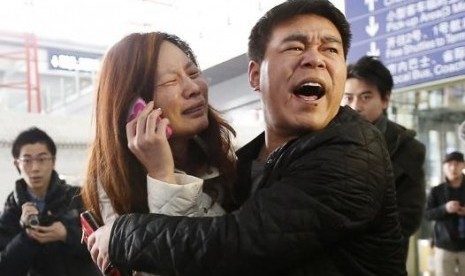 A relative (woman in white) of a passenger onboard Malaysia Airlines flight MH370 cries as she talks on her mobile phone at the Beijing Capital International Airport, March 8, 2014.