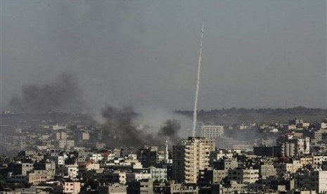 A rocket fired by Palestinian activists at southern Israel leaves a thin trail of white smoke, as smoke caused by explosions from Israeli forces' operations rises from buildings on the outskirts of Gaza City.  (File photo 2009)