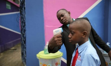 A school official takes a pupil's temperature using an infrared digital laser thermometer in front of the school premises, at the resumption of private schools, in Lagos in this September 22, 2014 file photo.