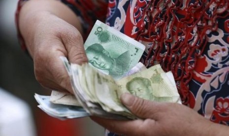 A vegetable vendor holds a stack of Chinese yuan banknotes at a morning market in Shenyang, Liaoning province June 10, 2014.