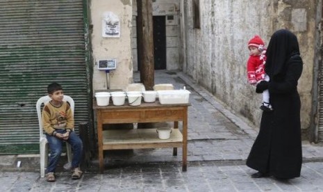 A woman carries a child as she walks past a boy selling yogurt along a street in Aleppo's Bab al-Hadeed district December 10, 2014.