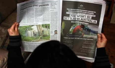 A woman reads a newspaper containing an advertisement (R) publicising the Australian government's new policy on asylum seekers arriving by boat, in Sydney August 2, 2013.