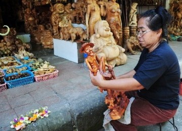 A worker sandpapers a wooden statute in Ubud, Bali (illustration).