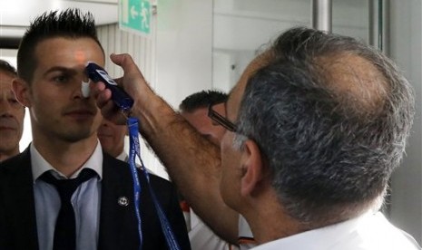 Airport physician Dr. Bargain (right) demonstrates the use of a thermometer to highlight measures to screen passengers for the Ebola virus, at the Charles de Gaulle airport, north of Paris, France, Friday, Oct. 17, 2014. 