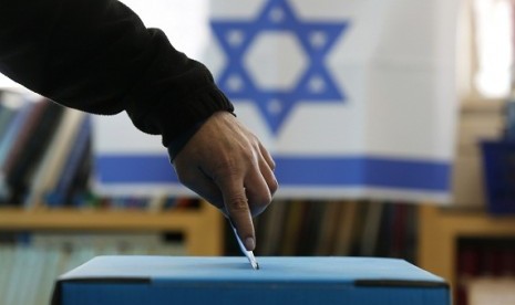 An Israeli flag is seen in the background as a man casts his ballot for the parliamentary election at a polling in the West Bank Jewish settlement of Ofra, north of Ramallah January 22, 2013. 