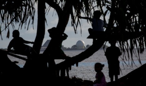 Anak-anak bermain di sebuah pohon di Ebeye berlatar belakang Ronald Reagan Ballistic Missile Defense Test Site (tempat pengujian rudal) di Kwajalein.