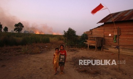 Anak-anak berpose di halaman rumah dengan latar belakang kebakaran lahan gambut di Kecamatan Bati-Bati, Kabupaten Tanah Laut, Kalimantan Selatan, Ahad (1/9/2019). 