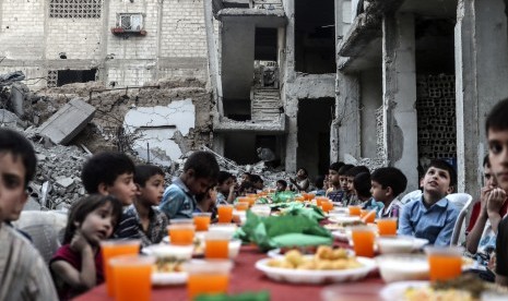 Anak-anak duduk menunggu iftar atau buka puasa di samping puing-puing dan reruntuhan bangunan, di Douma, Suriah, 17 Juni 2017.