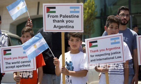 Anak-anak lelaki Palestina memegang spanduk di depan kantor perwakilan Argentina di kota Ramallah, Tepi Barat, Rabu (6/6). Argentina telah membatalkan pertandingan persahabatan melawan Israel menyusul protes oleh kelompok pro-Palestina.