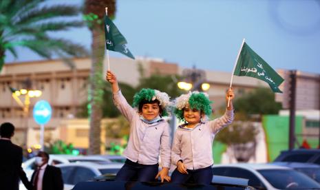 Anak-anak Saudi tersenyum gembira mengibarkan bendera negaranya. Arab Saudi mengejar jumlah kunjungan ziarah umroh dan wisata tahun ini 