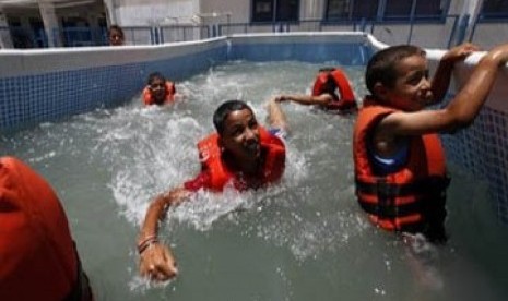 Anak-anak tengah menikmati berenang di kolam plastik di kemah musim panas milik PBB.