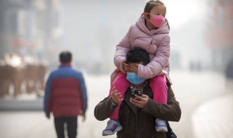  Anak perempuan mengenakan masker masker di atas gendongan seorang pria sambil menyusuri jalanan di Beijing, China, Selasa (28/1). Kematian akibat corona pertama terjadi di luar Wuhan, yakni di Beijing. 