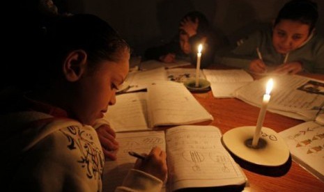 Anak sekolah Palestina mengerjakan pekerjaan rumah dengan penerangan lilin akibat pemadam listrik.