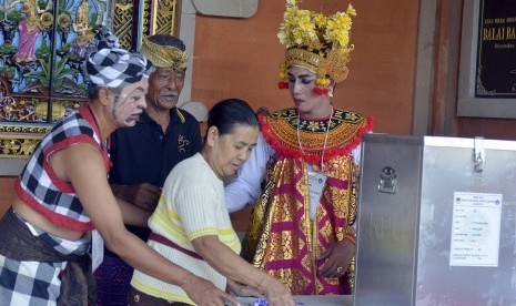 Anggota Kelompok Penyelenggara Pemungutan Suara (KPPS) yang mengenakan busana penari dan pelawak Bali membantu pemilih saat pemungutan suara Pilkada Serentak di Desa Penarungan, Kabupaten Badung, Bali, Rabu (9/12). 