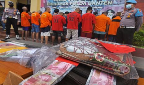 Anggota Polisi mengawasi sejumlah tersangka dan barang bukti kasus-kasus perjudian saat ekspos pemberantasan judi di Mapolda Banten, di Serang, Jumat (12/8/2022). Polda Banten berhasil menangkap 24 bandar dan pemain judi beserta barang bukti 20 unit ponsel yang digunakan untuk mengakses situs judi online serta uang sebesar Rp8,3 juta. 