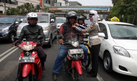   Anggota polwan Bripka Novi memperbaiki tali helm pengendara motor di lampu merah Bundaran HI, Jakarta Pusat, Senin (25/11).  (Republika/Yasin Habibi)