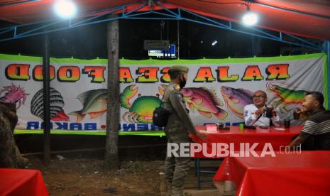 Anggota Satpol PP Kota Bogor menegur warga yang makan di warung saat penerapan jam malam di jalan Pajajaran, Kota Bogor, Jawa Barat, Selasa (1/9/2020). Pemerintah Kota Bogor memberlakukan jam malam mulai pukul 21.00 WIB dengan membatasi aktivitas warga di luar sebagai upaya menekan tingginya angka penularan COVID-19 di wilayah zona merah Kota Bogor dalam masa Pembatasan Sosial Berskala Mikro dan Komunitas (PSBMK).