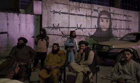 Anggota Taliban duduk di depan mural yang menggambarkan seorang wanita di balik kawat berduri di Kabul, Afghanistan, Selasa, 21 September 2021.