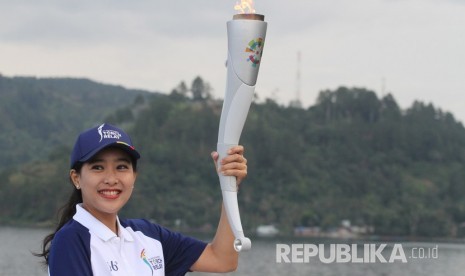 Artis Olivia Zalianty memegang obor Asian Games 2018 dengan latar belakang Danau Toba, di Parapat, Simalungun, Sumatera Utara, Rabu (1/8). 