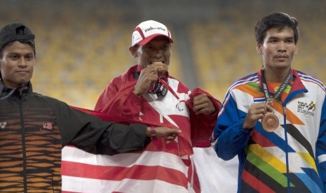 Atlet Indonesia Endi Nurdin Tine (tengah) menggigit medali emas yang diraihnya setelah menjuarai nomor lari 800 meter putra Asean Para Games XI Kuala Lumpur, di Stadion Bukit Jalil, Kuala Lumpur, Malaysia, Selasa (19/9). 